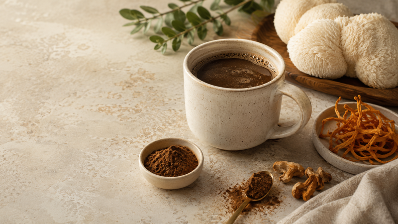 A ceramic mug of dark coffee beside a whole dried lion's mane mushroom and ground mushroom coffee powder on a stone surface.